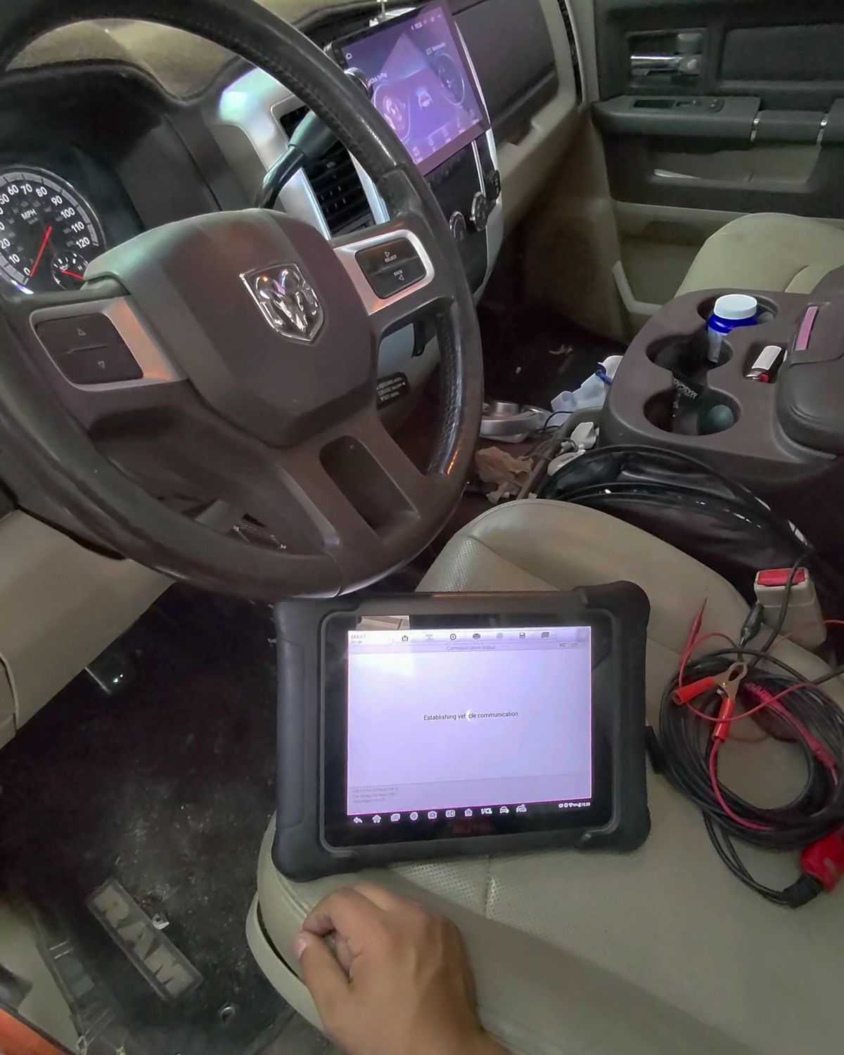 A diagnostic scan tablet on the seat of a pickup truck, with test leads beside it